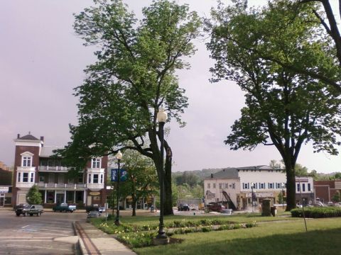 1985 Ford LTD Crown Victoria - Town square scene with historic buildings and trees, some vehicles are present.