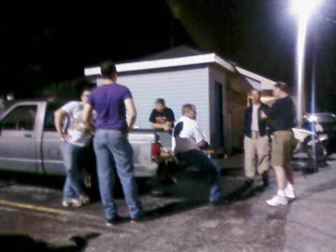 1985 Ford LTD Crown Victoria - A group of friends gather near a pickup truck and a building at night.