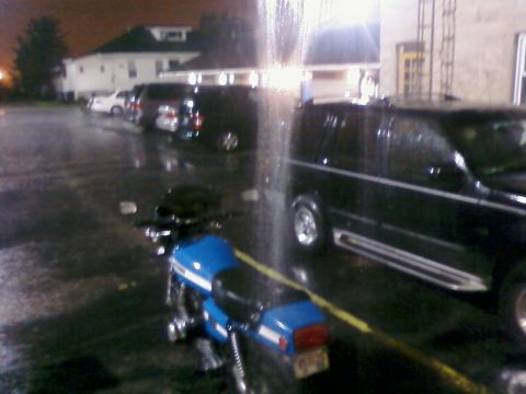 1985 Ford LTD Crown Victoria - A blue motorcycle is parked on a wet lot at night, with a black van nearby.