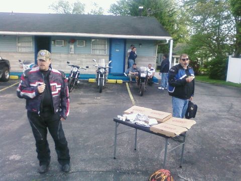 1985 Ford LTD Crown Victoria - Several motorcycles are parked in front of a motel where a group of people are gathered, some eating pizza.