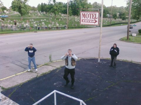 1985 Ford LTD Crown Victoria - Three people stand in a parking lot near a motel sign that reads 'MOTEL ENTER' with an arrow indicating 'ENTER'.