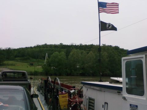 1985 Ford LTD Crown Victoria - Vehicles on a ferry with flags flying against a backdrop of trees and a cloudy sky.