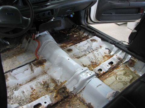 2003 Ford Crown Victoria - The floor pan of a 2003 Ford Crown Victoria shows significant rust and debris after carpet removal.