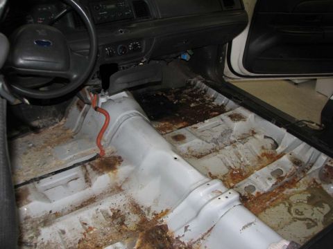 2003 Ford Crown Victoria - The interior of a 2003 Ford Crown Victoria shows significant rust and damage to the floor pans.