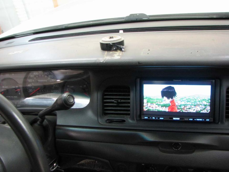 Dashboard of a 2003 Ford Crown Victoria with a screen displaying anime, showing the steering wheel and gear shift