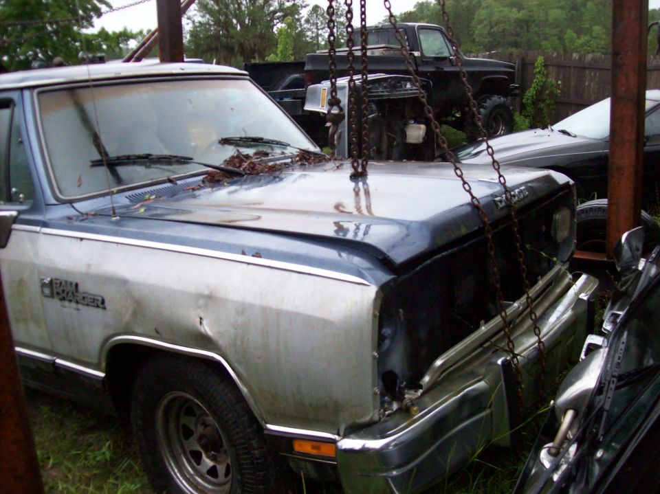 1988 Dodge Power Ram pickup truck with dented fender, hood open, chains attached. Another truck is visible behind it