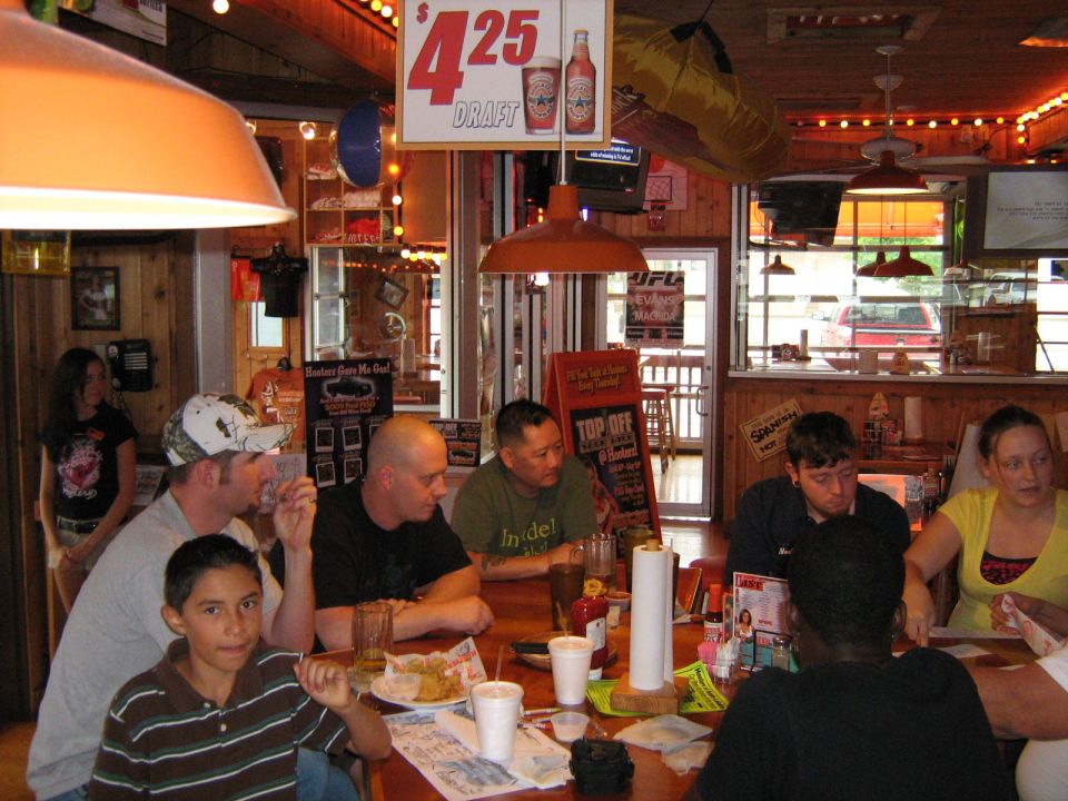 People gathered around a table inside a restaurant with a sign for $4.25 draft beer overhead