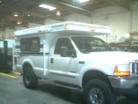 2000 Ford F-250 - White 2000 Ford F-250 pickup truck equipped with a camper shell is parked inside a building.