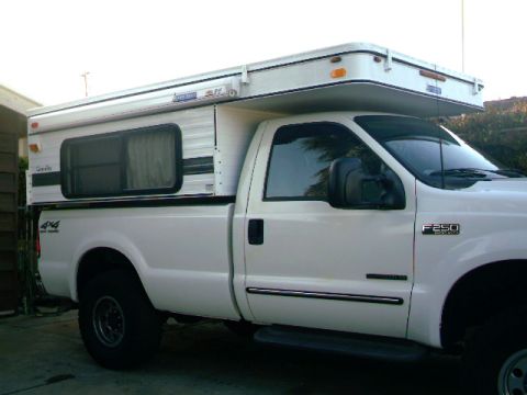 2000 Ford F-250 - This 2000 Ford F-250 pickup truck is equipped with a white camper shell, seen from the side.