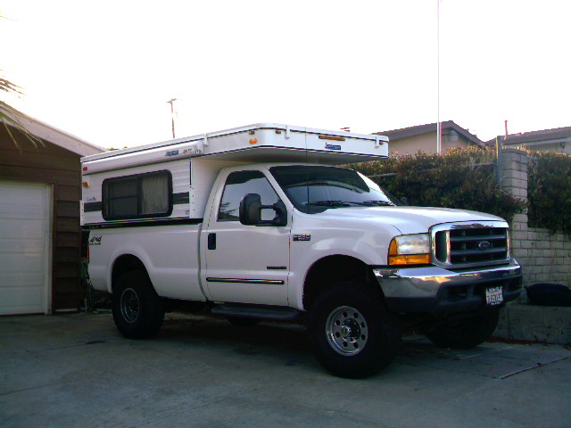 White pickup truck with a camper shell parked in a driveway. The truck has a chrome grille and bumper