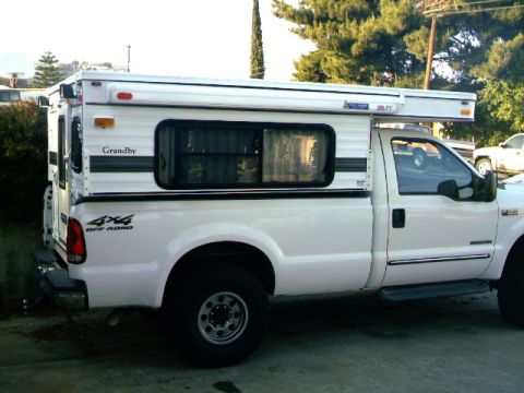 2000 Ford F-250 - A white 2000 Ford F-250 pickup truck is equipped with a Grandby camper shell for off-road adventures.