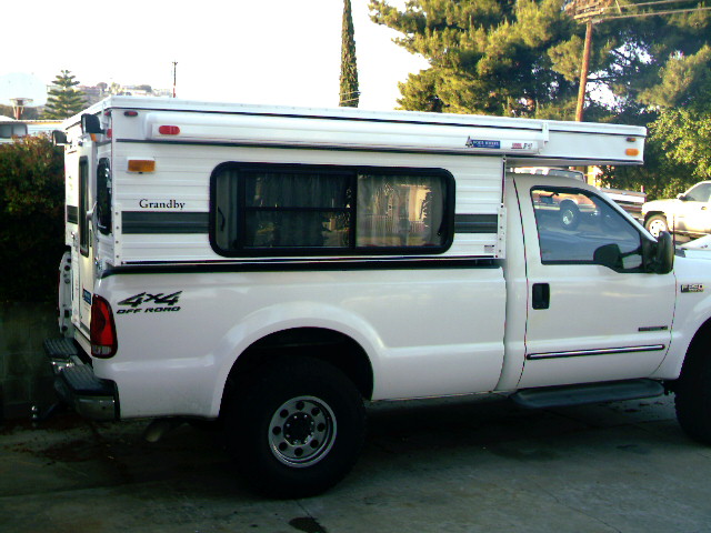 White 2000 Ford F-250 pickup truck with a Grandby camper shell, side view