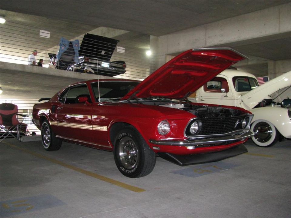 Red 1969 Ford Mustang Mach 1 with hood open, parked next to a white pickup truck