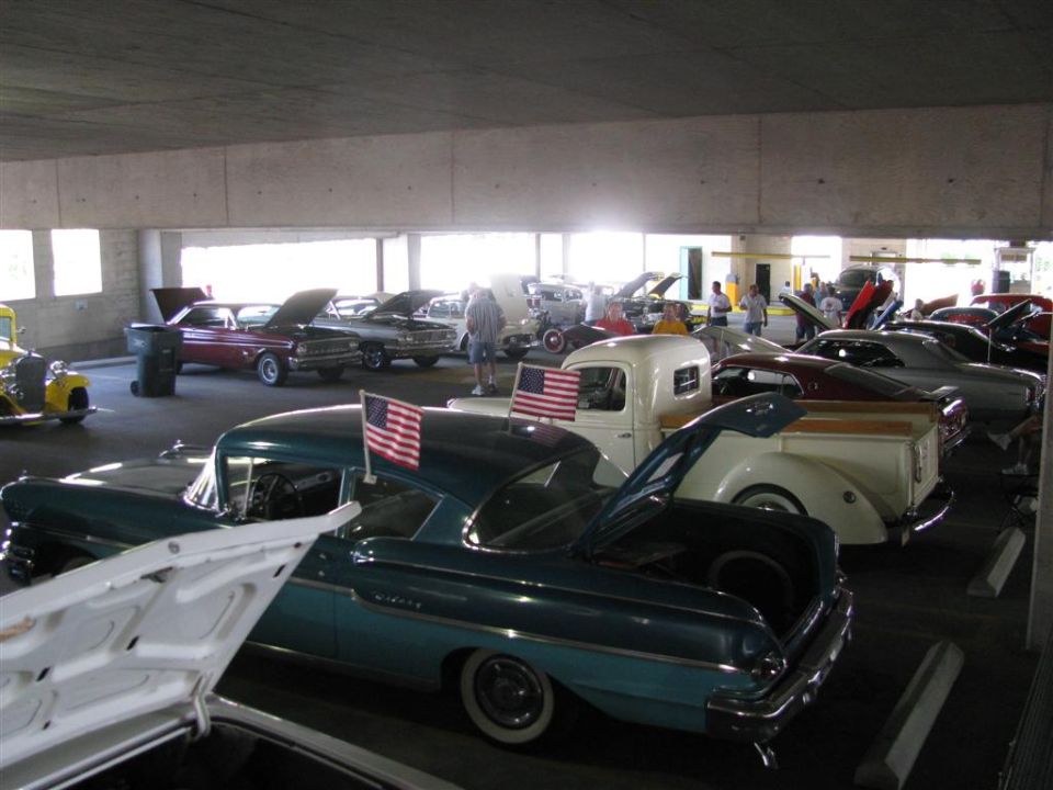 Cars parked inside a garage, some with hoods open. American flags on two cars
