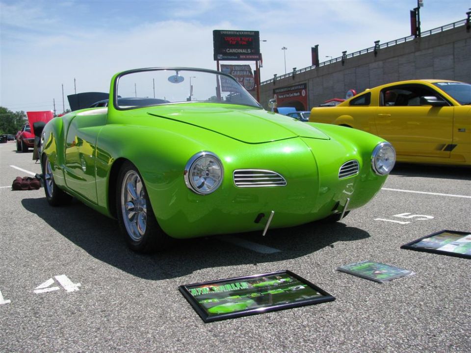 Green convertible sports car with chrome accents and aftermarket wheels, parked on asphalt with display photos on the ground
