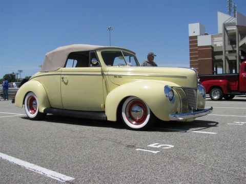 2003 Mercury Marauder - A classic yellow 1940 Ford convertible is parked at an outdoor event with a red pickup truck nearby.