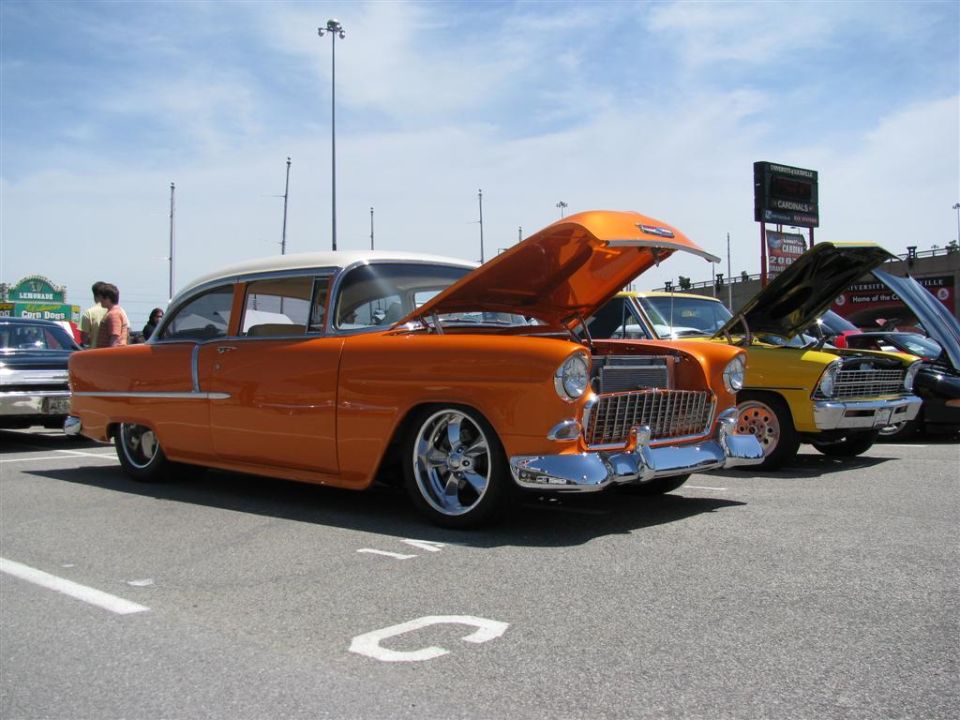 Orange and white 1955 Chevrolet sedan with hood open, chrome grille, and custom wheels