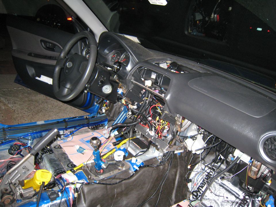 Interior of a 2007 Subaru Impreza with dashboard removed, showing extensive wiring and sound dampening material on the floor