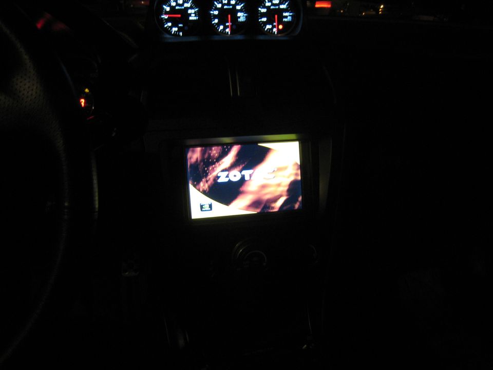 Car interior at night, showing dashboard gauges and a screen displaying "ZOT"