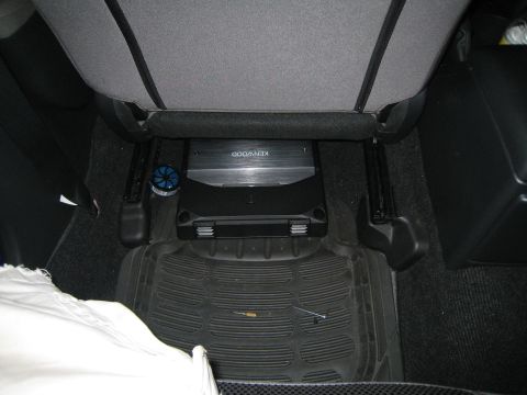 2007 Subaru Impreza - A Kenwood amplifier is installed under the rear seats of a car, resting on a rubber floor mat.