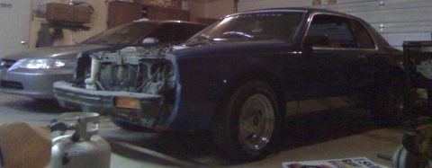 2006 Ford E350 - A dark blue coupe, possibly from the 1970s, is undergoing repairs in a garage, with a silver sedan visible behind it.