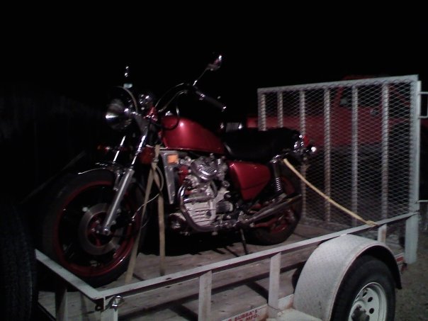 Red Honda motorcycle tied down with yellow straps on a utility trailer at night