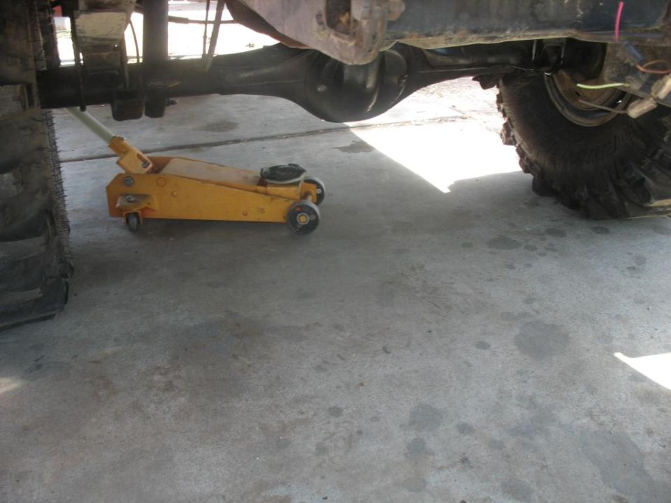 Yellow floor jack under a lifted 4x4 rear axle on a concrete garage floor