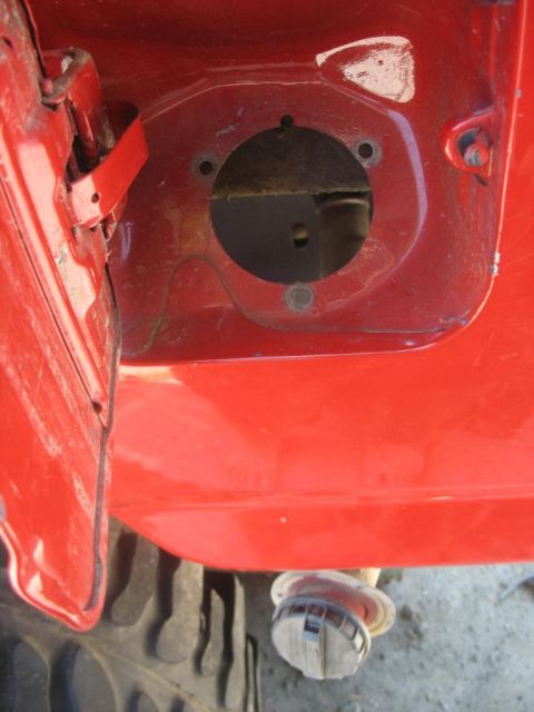 1987 Ford Bronco - Close-up of a red vehicle's fuel filler opening, with a fuel cap visible.
