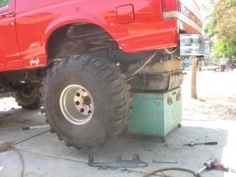 1987 Ford Bronco - The rear section of a red 4x4 SUV is shown with a large fuel tank suspended beneath it.