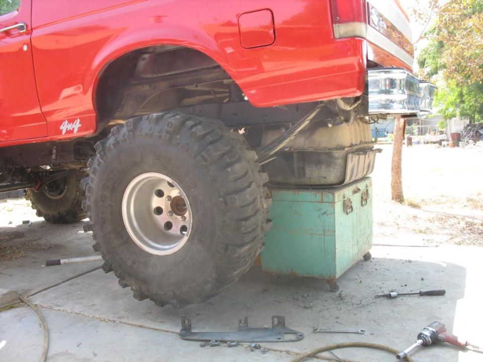 Lifted red Ford 4x4 on a toolbox with fuel tank dropped for removal in a driveway