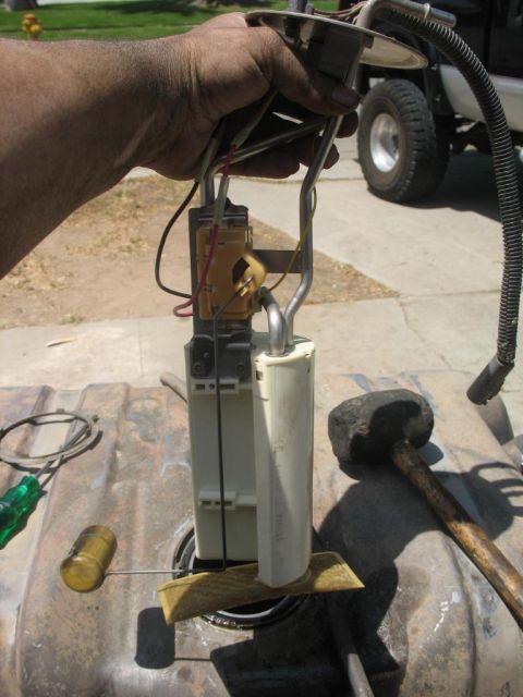1987 Ford Bronco - A person holds a fuel pump assembly over a fuel tank, with a truck visible in the background.