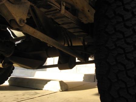 1984 Ford Bronco - The underside of a vehicle is captured, focusing on the suspension components and a large tire.