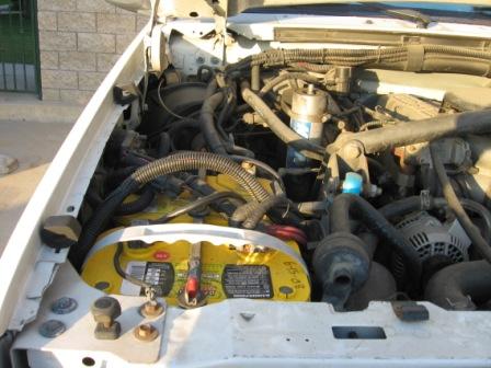 1984 Ford Bronco - Engine bay of a white vehicle, showing a yellow Optima battery and various engine components.