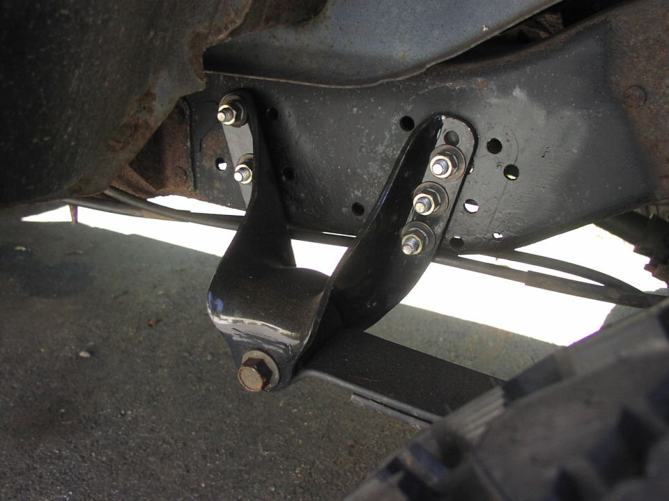 Leaf spring hanger bracket bolted to frame rail, with part of a tire visible