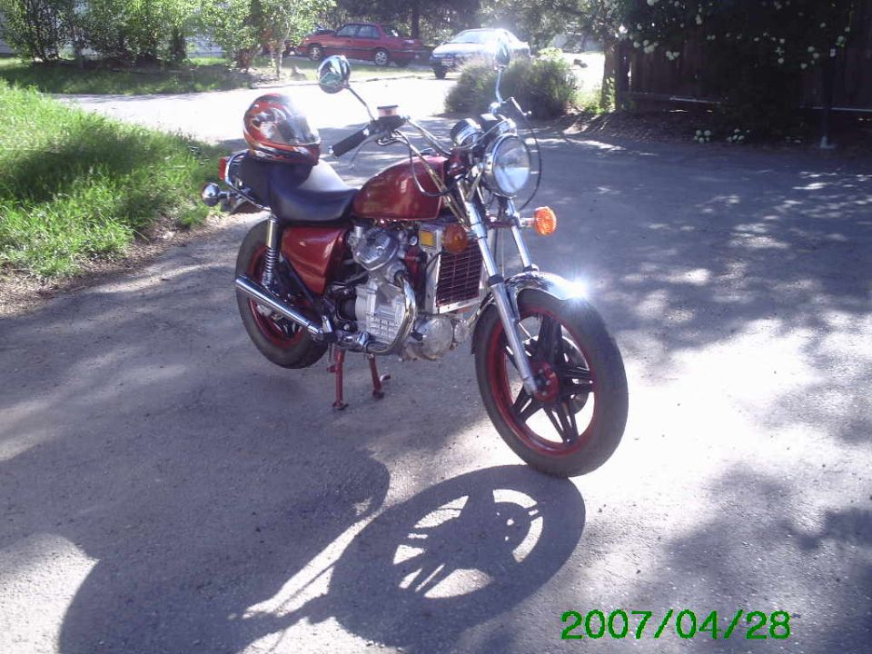 Maroon Honda cruiser motorcycle with red helmet parked on a gravel driveway