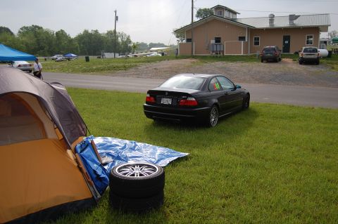 2002 BMW M3 - A black 2002 BMW M3 is parked on the grass next to a tent at a track event.