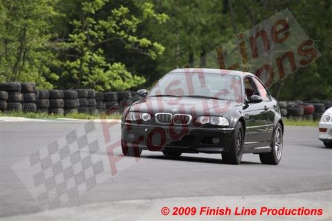 2002 BMW M3 - A black BMW M3 navigates a turn on a race track, with tire barriers lining the course.