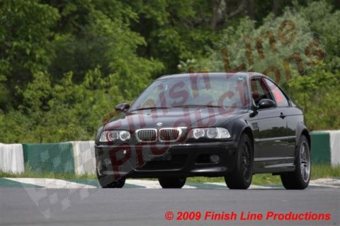 2002 BMW M3 - A black 2002 BMW M3 coupe is seen on a race track with green trees in the background.