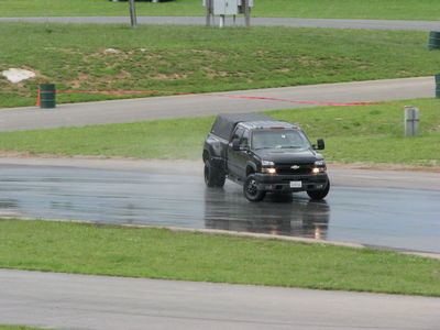 2002 BMW M3 - Black Chevrolet Silverado pickup truck with camper shell driving on a wet track.