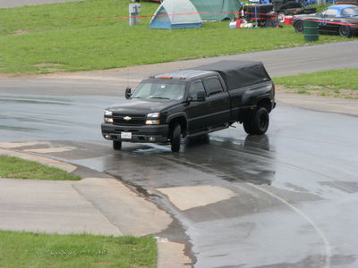 2002 BMW M3 - A black pickup truck with a soft tonneau cover drives on a wet surface, with tents and another vehicle visible in the background.