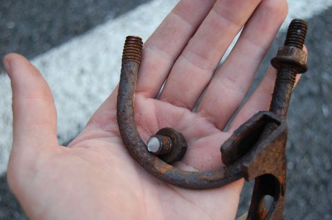 1994 Ford Bronco - A corroded exhaust hanger and hardware are held in a person's palm against a blurred asphalt background.