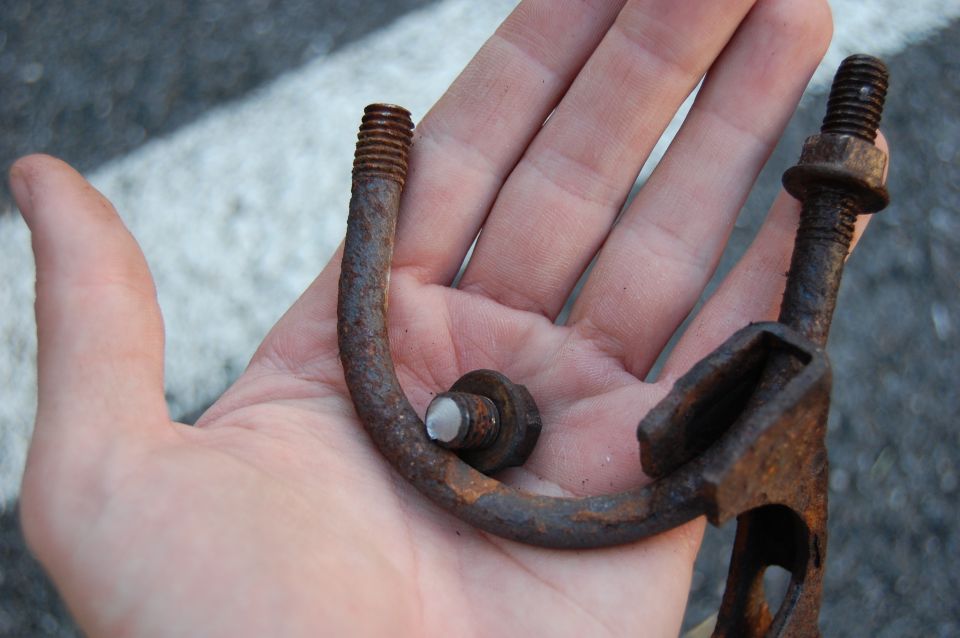 Rusted exhaust hanger with bolt and nut held in a hand