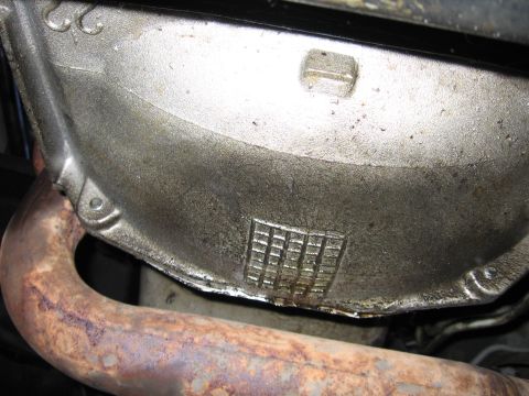 1990 Ford Bronco - Underside view of a vehicle's oil pan and exhaust pipe, showing signs of wear and tear.