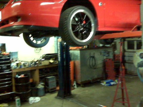 2004 Ford Mustang - A red 2004 Ford Mustang is shown on a lift in a garage, with its front end and wheel clearly visible.