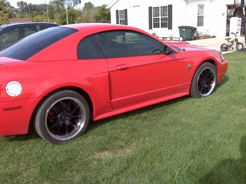2004 Ford Mustang - A red 2004 Ford Mustang is parked on the grass in front of a white house.