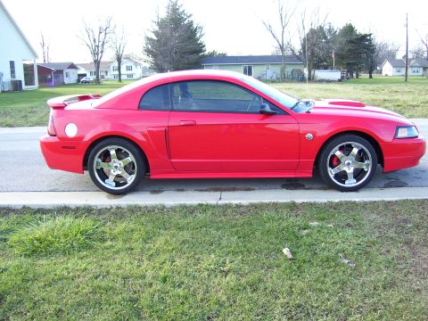 2004 Ford Mustang - This red 2004 Ford Mustang coupe is shown from the side, parked on a suburban street.