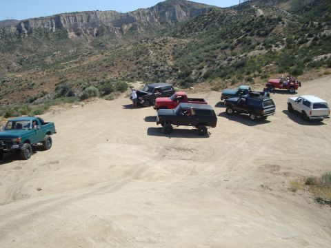 1986 Ford Bronco - A group of off-road vehicles are gathered on a dirt road in a dry, mountainous landscape.