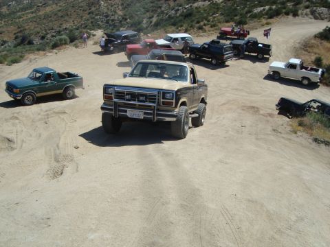 1986 Ford Bronco - Multiple off-road vehicles gather on a dusty trail, with a tan 1980 Ford Bronco prominently in the foreground.