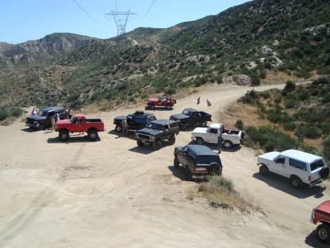 1986 Ford Bronco - A group of off-road vehicles, including a 1986 Ford Bronco, are gathered on a dusty trail in a mountainous area.
