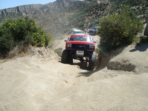 1986 Ford Bronco - This red SUV is navigating a challenging off-road trail with other vehicles in the distance.